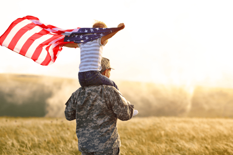 A son being held by his military father while holding the American flag